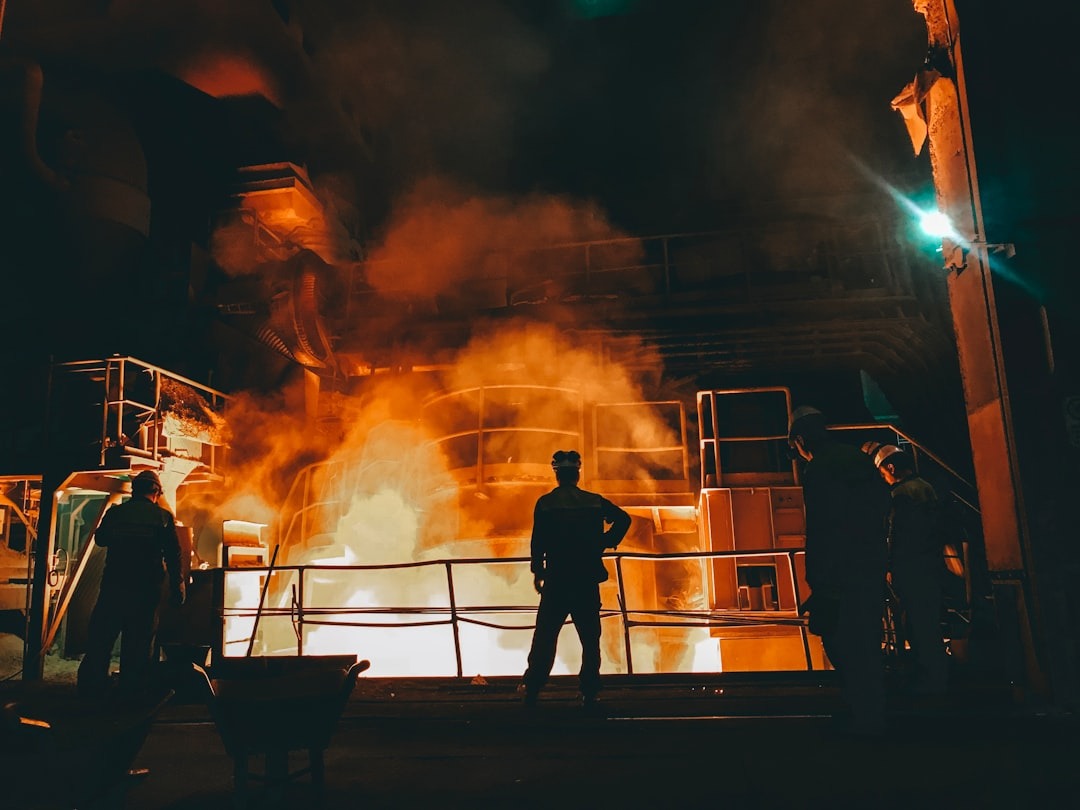 Four workers observe molten metal in an industrial foundry.